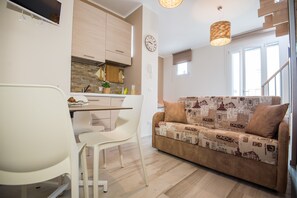 Une cuisine moderne avec un coin repas, un canapé recouvert d’un tissu à motifs et une horloge au mur.