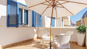 A sunlit patio with white chairs, a table, and a large umbrella. - San Vito Lo Capo with style and relaxation .. (San Vito Lo Capo)