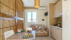A compact kitchen with a dining area, featuring a bamboo partition, a woven light fixture, and a sofa with a patterned cover. - San Vito Lo Capo with style and relaxation .. (San Vito Lo Capo)