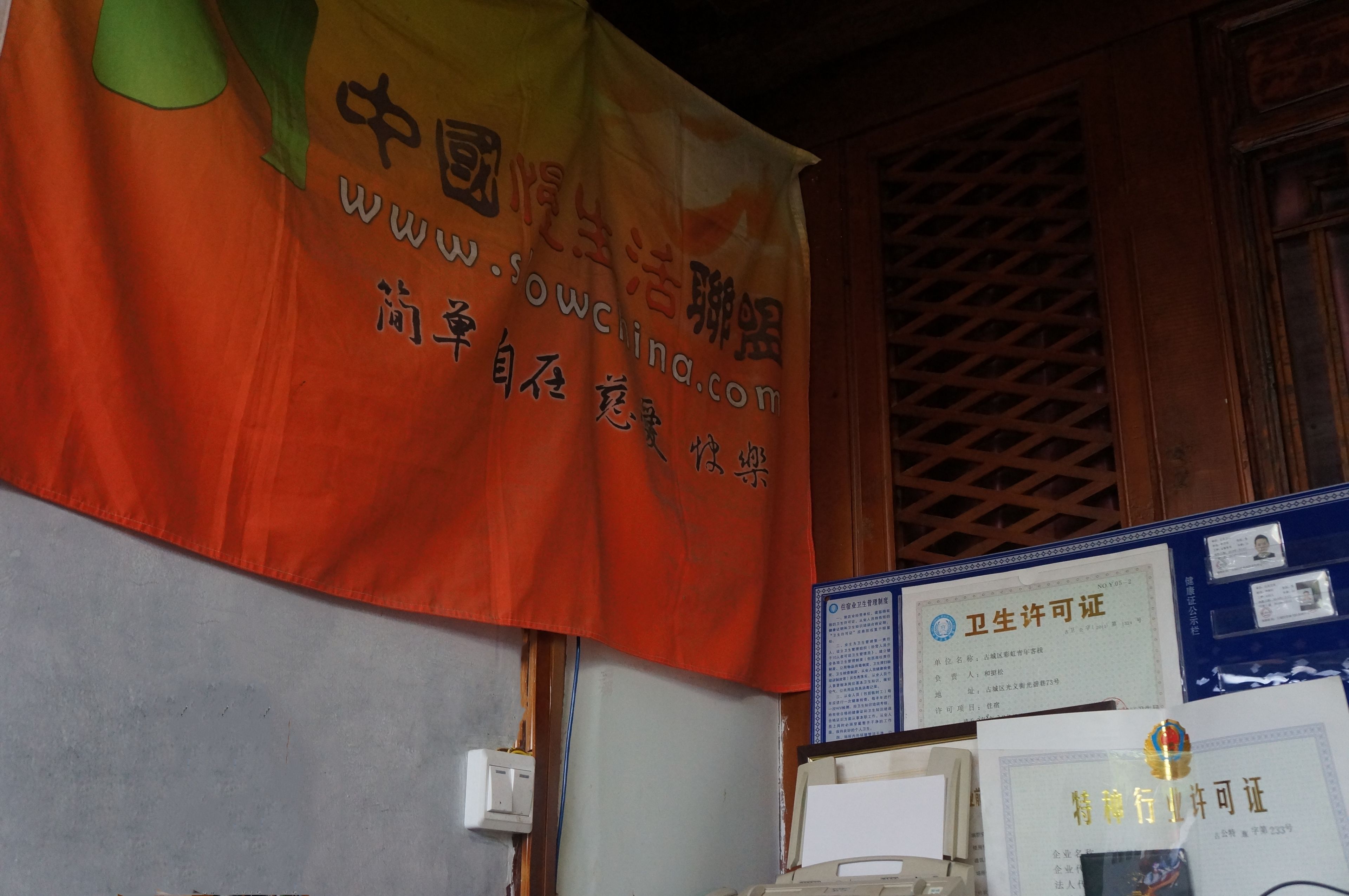 A banner with Chinese text and a website URL, a framed certificate, and a small desk with papers.