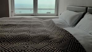 A hotel room with a large bed, a window with a view of the sea, and a headboard.