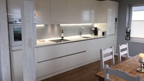 A modern kitchen with white cabinets, a built-in oven, a sink, and a coffee maker.