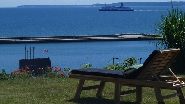 A lounge chair by a waterfront with a ship in the background.