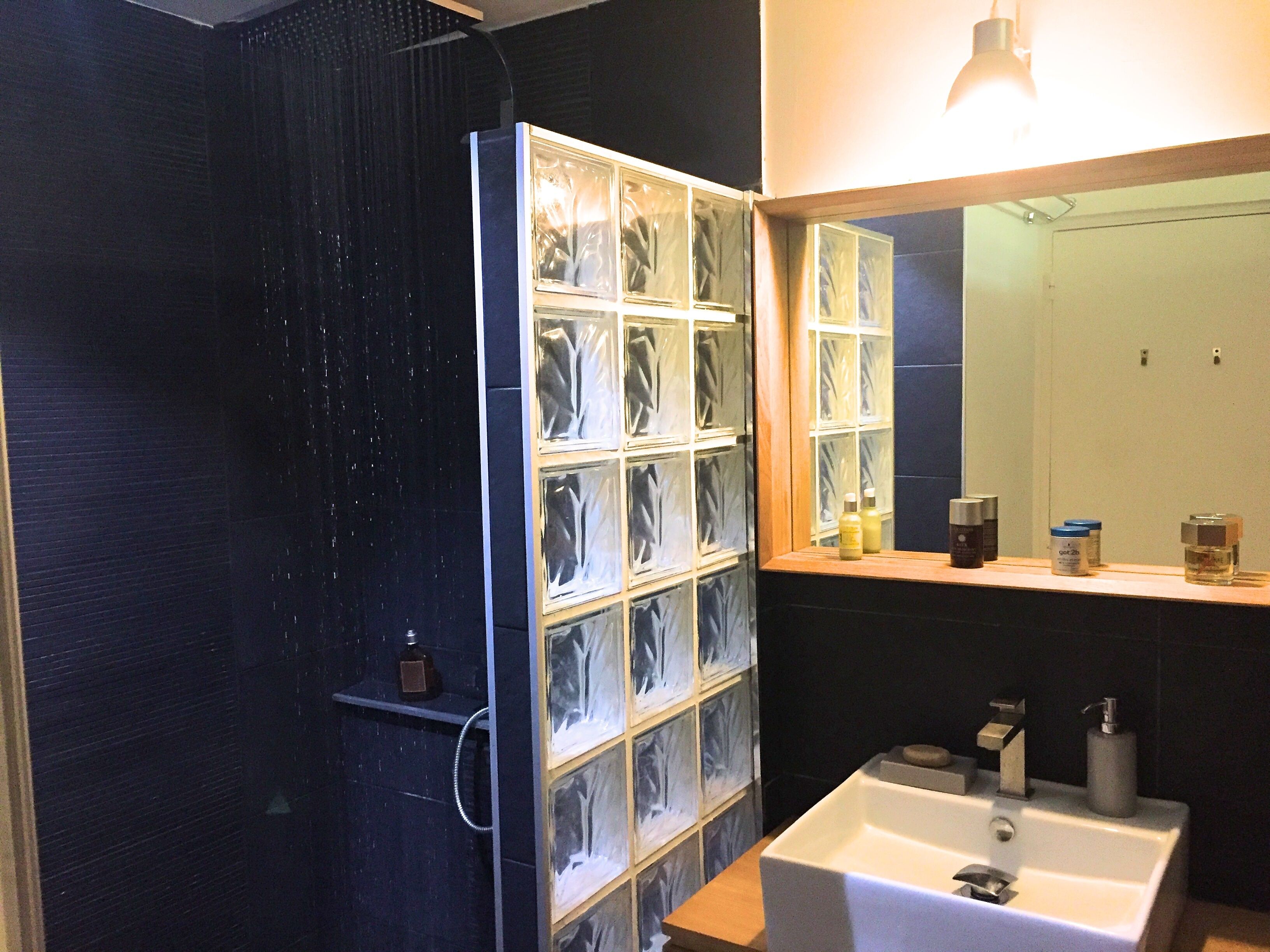 Une salle de bain avec une douche à parois de verre, un lavabo avec un miroir et des articles de toilette posés sur le comptoir.