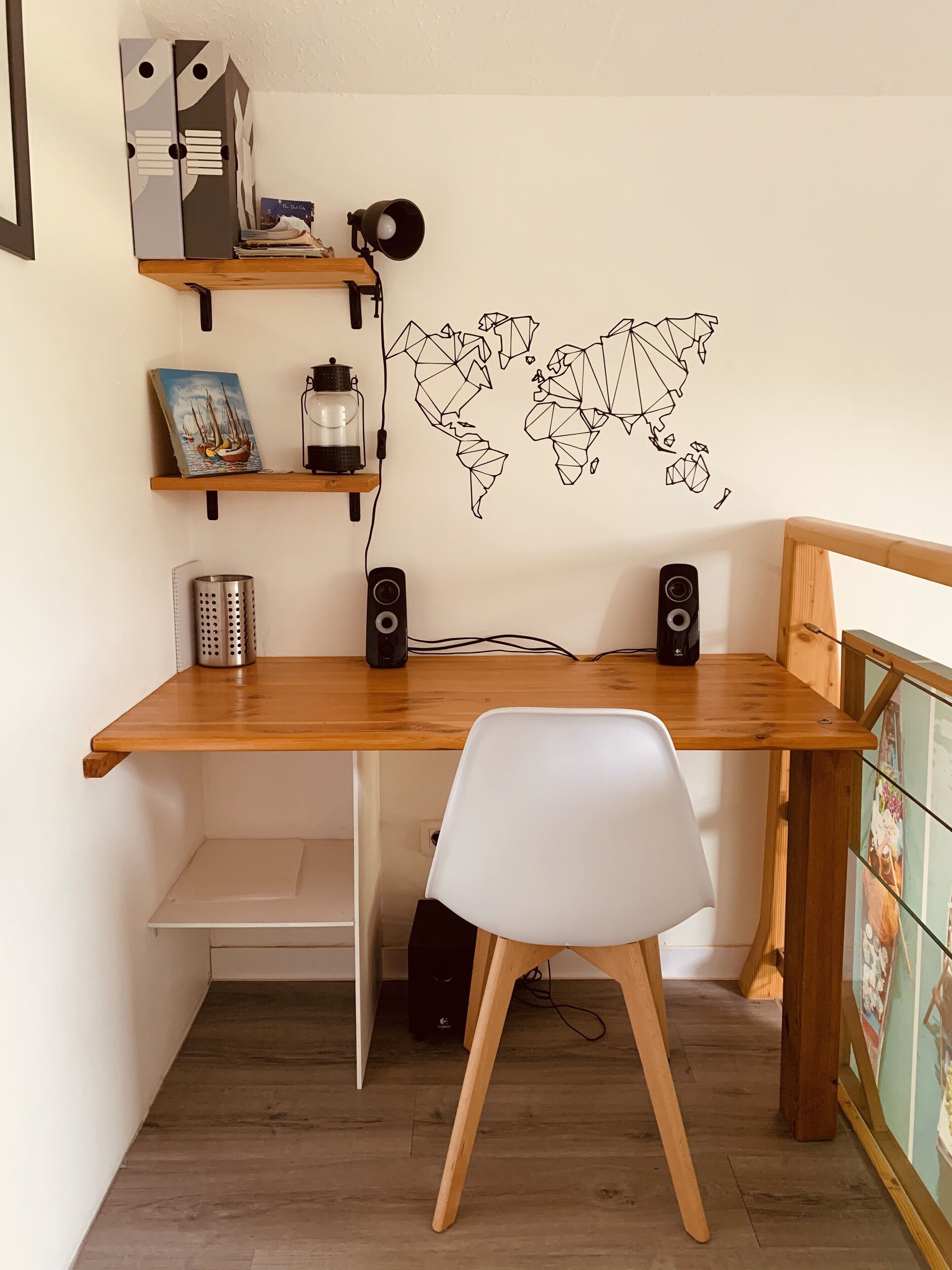 A wooden desk with two black speakers, a white chair, and a world map wall decal.