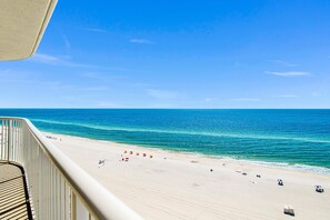 A beach view from a balcony with a railing, a sandy beach, and the ocean. - Beachfront 2BR @ Tradewinds • Sleeps 6 • Stunning Gulf Views • Pool Access (Orange Beach)