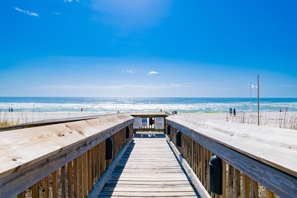 A wooden boardwalk leading to a beach with clear skies and ocean views.