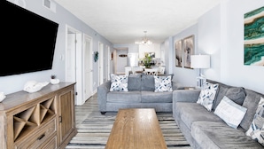 A living room with a grey sofa, wooden coffee table, and a TV on the wall. - Beachfront 2BR @ Tradewinds • Sleeps 6 • Stunning Gulf Views • Pool Access (Orange Beach)