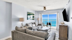 A living room with a grey sofa set, a wooden cabinet, and a flat-screen TV mounted on the wall. - Beachfront 2BR @ Tradewinds • Sleeps 6 • Stunning Gulf Views • Pool Access (Orange Beach)