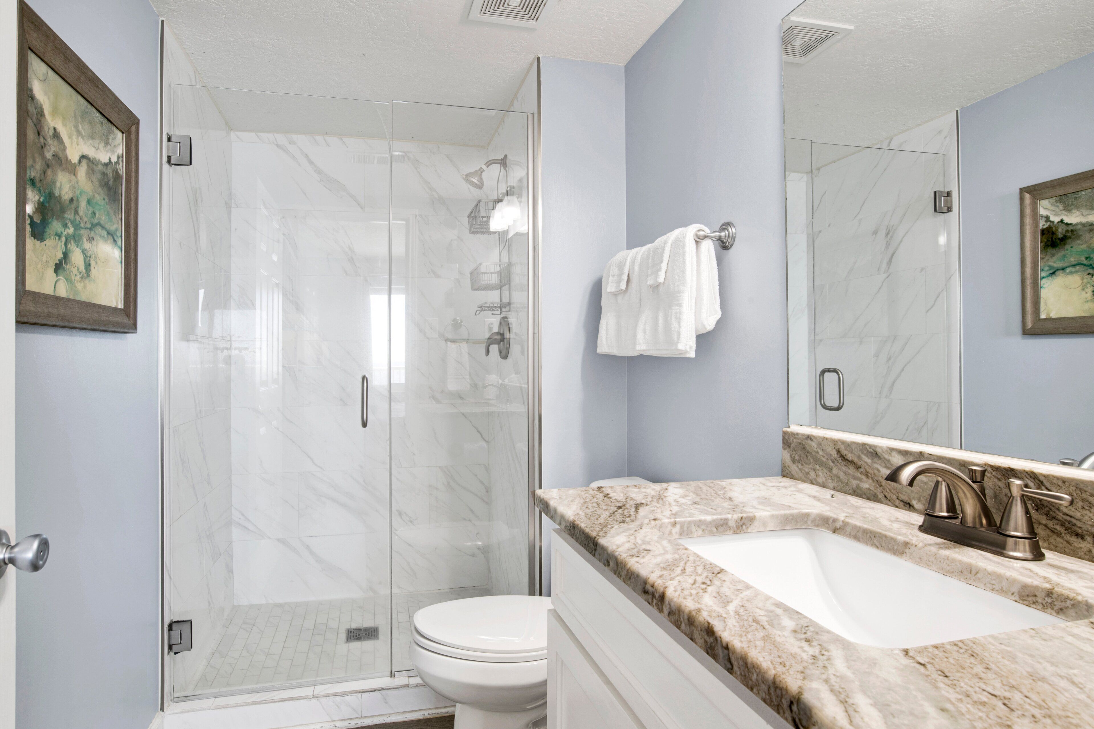 A bathroom with a glass-enclosed shower, a white toilet, and a marble countertop with a sink and faucet.