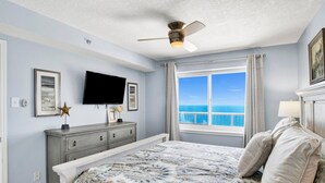 A bedroom with a bed, a ceiling fan, a TV, a dresser, a window with a view of the ocean, and a framed picture on the wall. - Beachfront 2BR @ Tradewinds • Sleeps 6 • Stunning Gulf Views • Pool Access (Orange Beach)