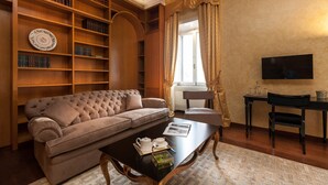 A living room with a sofa, a coffee table, a bookshelf, a television, and a window with curtains. - Prestigious Apartment Piazza Navona - Campo de' Fiori - Holiday in Rome (Roma)