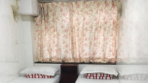 A room with two single beds, each with a wooden frame and white bedding. There is a small wooden nightstand between the beds, and a wall-mounted air conditioning unit above. - Capital Guesthouse (Kowloon)