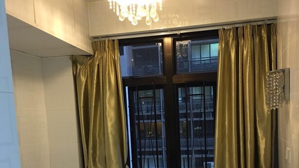 A small, single-bed room with a window, curtains, and a chandelier. - Capital Guesthouse (Kowloon)