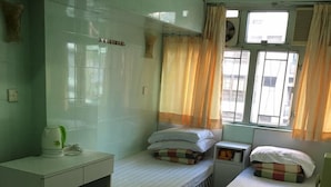 A dormitory room with two single beds, a desk, a chair, and a window with curtains. - Capital Guesthouse (Kowloon)