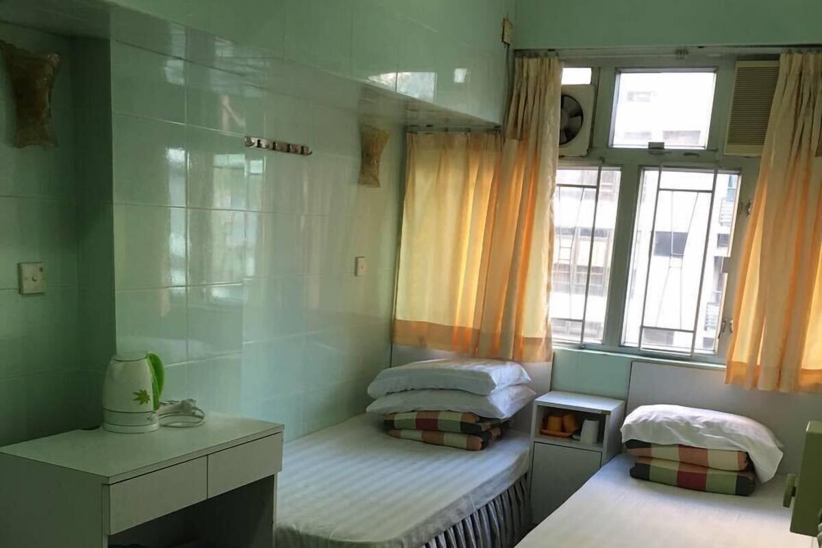 A dormitory room with two single beds, a desk, a chair, and a window with curtains.