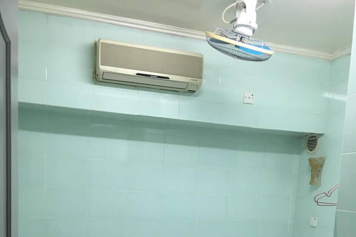 A small, clean room with two single beds, a bedside table, an air conditioning unit, and a ceiling fan.
