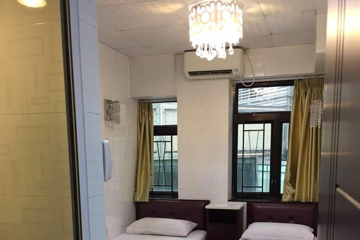 A hotel room with two beds, a chandelier, and large windows with curtains.