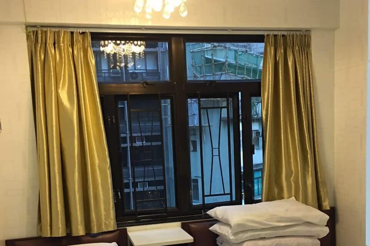 A hotel room with two beds, a nightstand, a window with curtains, and a chandelier.
