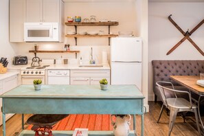 A compact kitchen with white appliances, a dining table with chairs, and a unique wall-mounted ski rack.