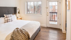 A bedroom with a large bed, a nightstand, a window, and a door. - Outpost: Pitchfork 2303 - Close to Snow King Mtn! (Jackson)