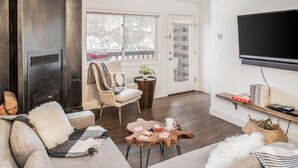 A cozy living room with a fireplace, a comfortable sofa, a coffee table with books and a cup, and a TV mounted on the wall. - Outpost: Pitchfork 2303 - Close to Snow King Mtn! (Jackson)