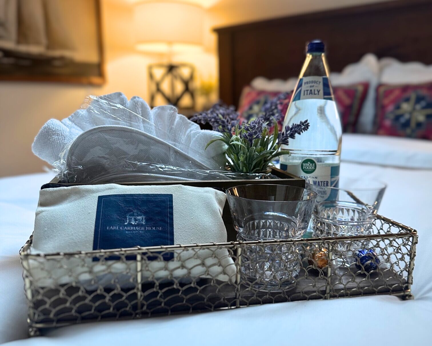 A hotel room with a neatly arranged bed, a bedside table with a bottle of water, a glass, and a small plant.