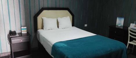 A hotel room with a bed, a nightstand, a desk, and a chair.