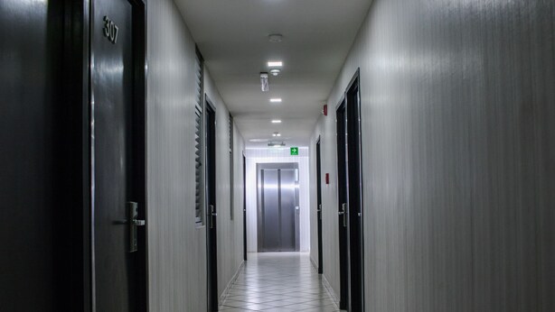 Un pasillo con puertas a ambos lados, piso de baldosas y un ascensor al final.