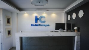 Una mesa de recepción de hotel con encimera de mármol, el logotipo de 'Hotel Careyes' y tres relojes en la pared.