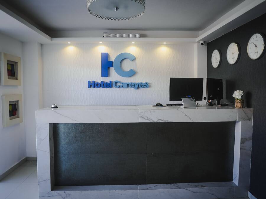 Una mesa de recepción de hotel con encimera de mármol, el logotipo de 'Hotel Careyes' y tres relojes en la pared.