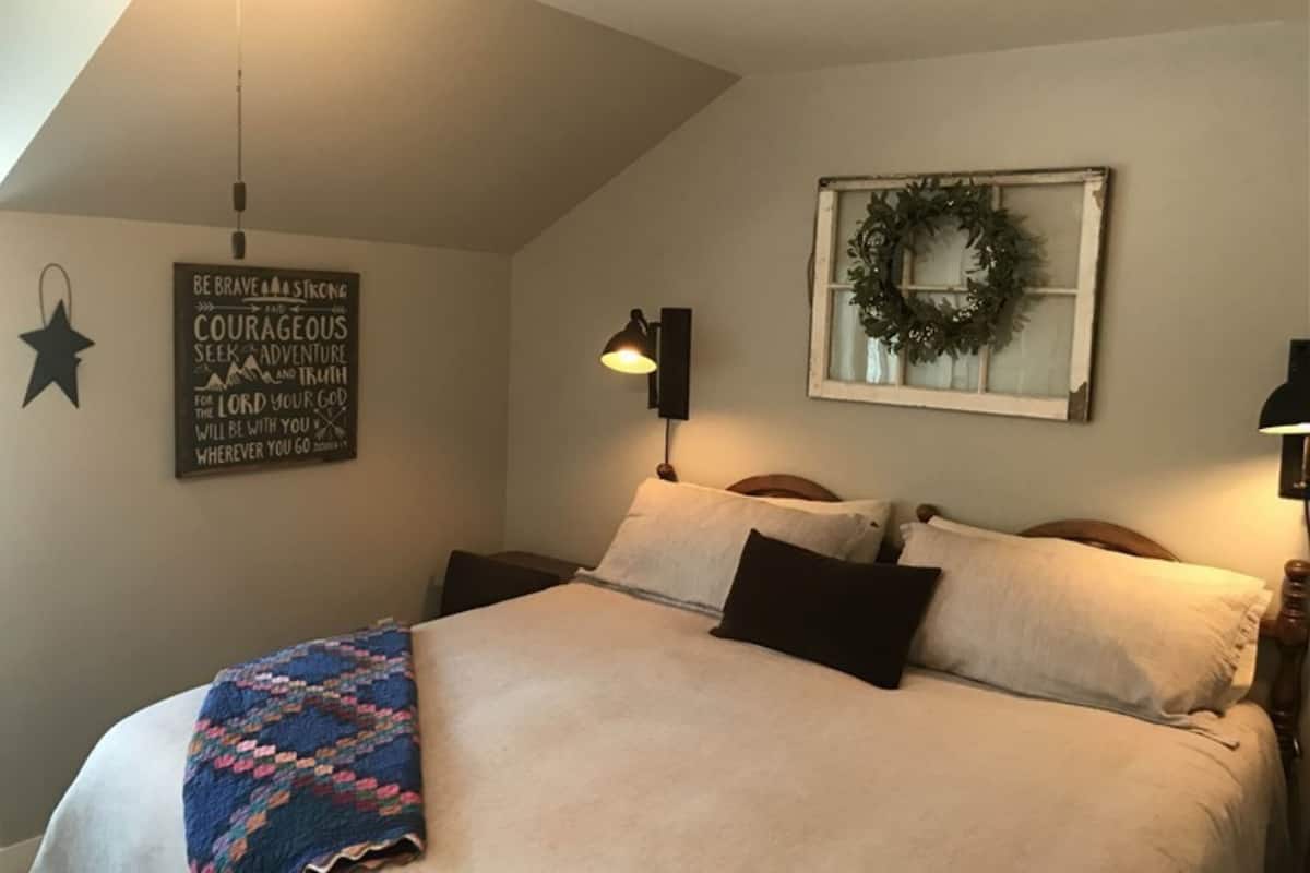 A bedroom with a bed, a wall-mounted star decoration, a motivational quote, a wreath, and a wall-mounted lamp.