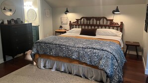 A bedroom with a large bed, a dresser, a nightstand, and a wall-mounted lamp. - Snowgoose Pond Bed & Breakfast (Palmer)