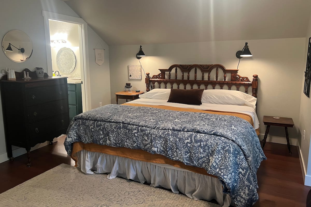 A bedroom with a large bed, a dresser, a nightstand, and a wall-mounted lamp.