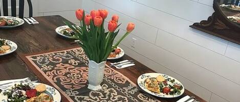 Une table à manger dressée avec des assiettes remplies de nourriture, un vase de tulipes et un chemin de table décoratif.
