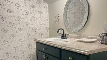 A bathroom with a sink, dark green cabinets, and a floral wallpaper pattern.