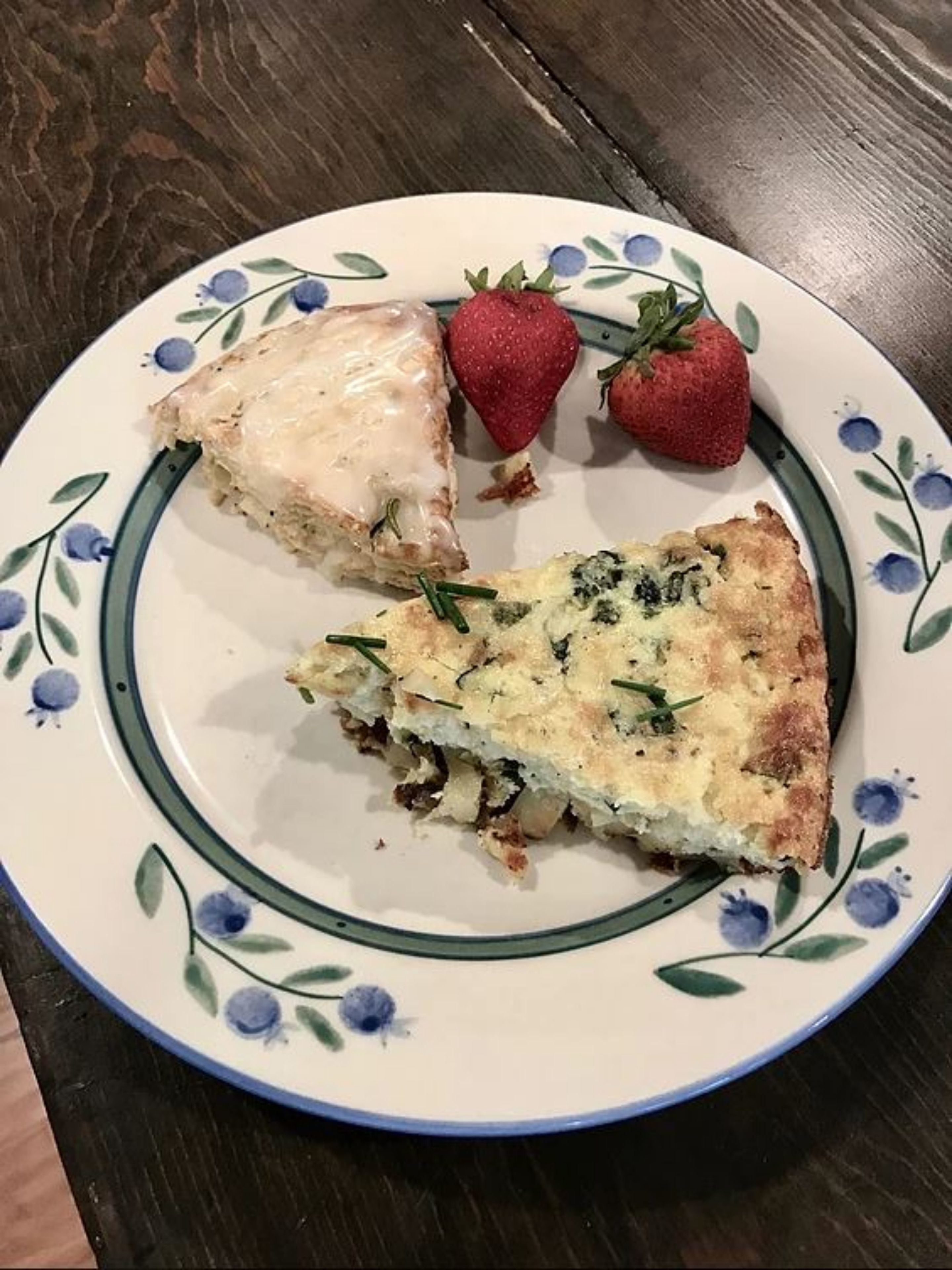 A plate with a slice of quiche and two strawberries on a floral-patterned plate.