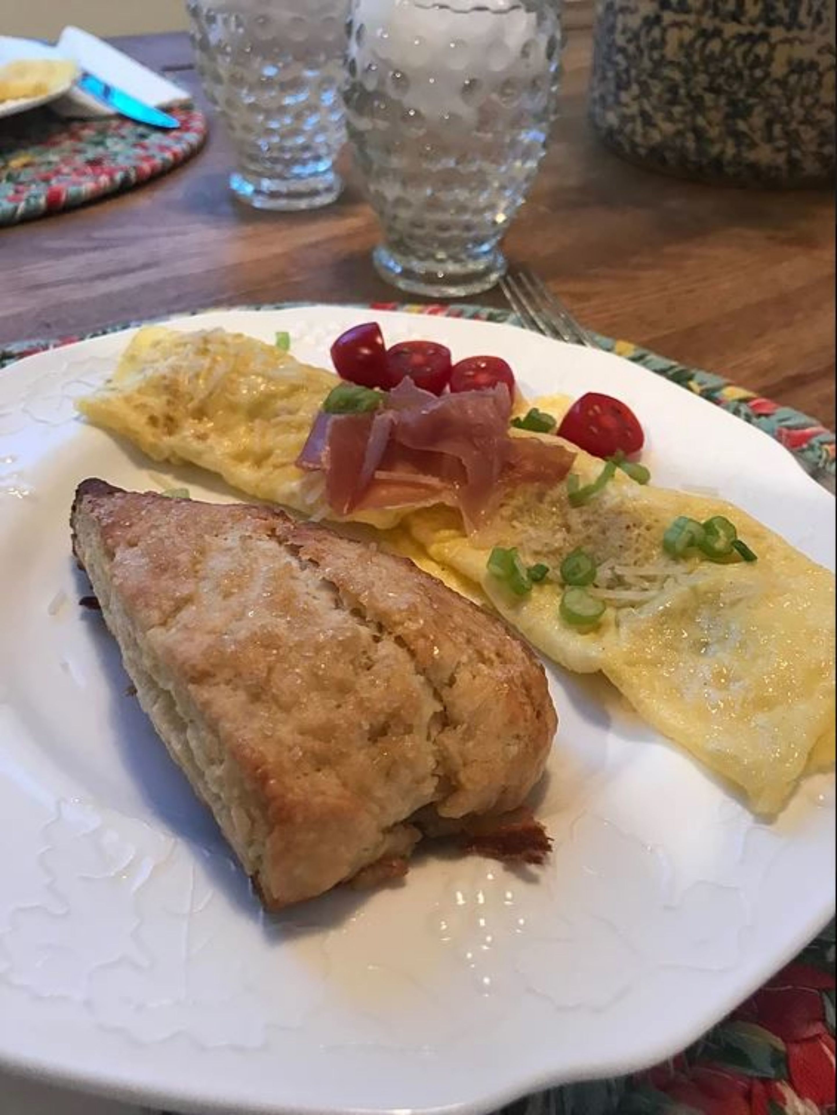 A plate with an omelette, prosciutto, cherry tomatoes, and a biscuit.