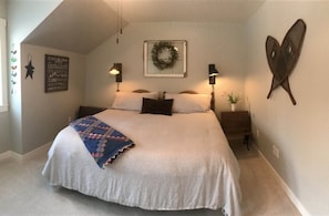 A bedroom with a large bed, two bedside tables with lamps, a wall-mounted wreath, and a star-shaped decoration.