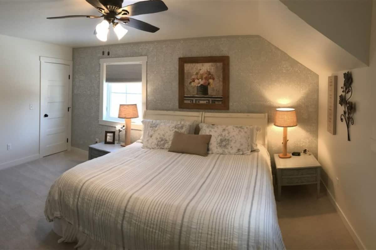 A bedroom with a bed, two bedside tables, a ceiling fan, a window, and a framed picture on the wall.
