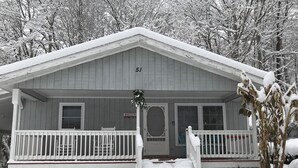 Una casa de madera con porche, número 51, rodeada de árboles cubiertos de nieve.