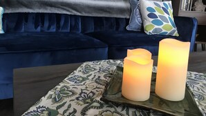 Un sofá azul oscuro con cojines estampados, una bandeja con velas y una lámpara decorativa.