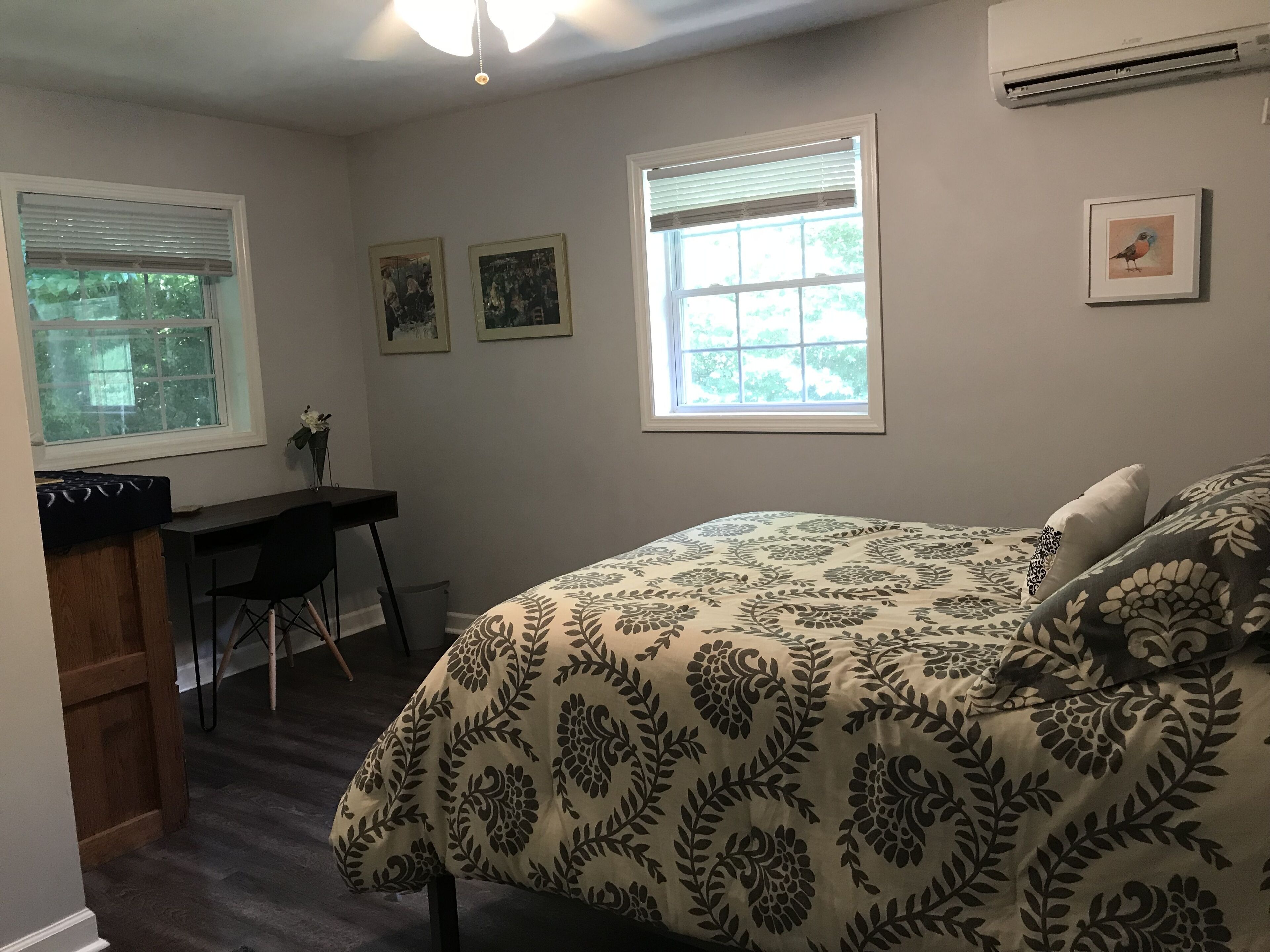 A bedroom with a bed, a desk, and two windows.
