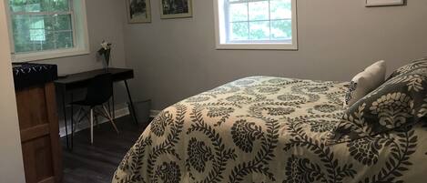 A bedroom with a bed, a desk, and two windows.