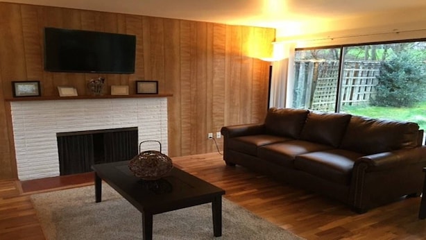 Una sala de estar con chimenea, un sofá de cuero y un televisor montado en la pared.