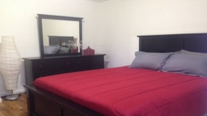 Un dormitorio con colcha roja, cabecero oscuro y espejo sobre un tocador.