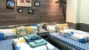 A hotel room with two beds, a wooden accent wall, and a small table with a phone and a sign. - Hong Kong Hostel (Kowloon)
