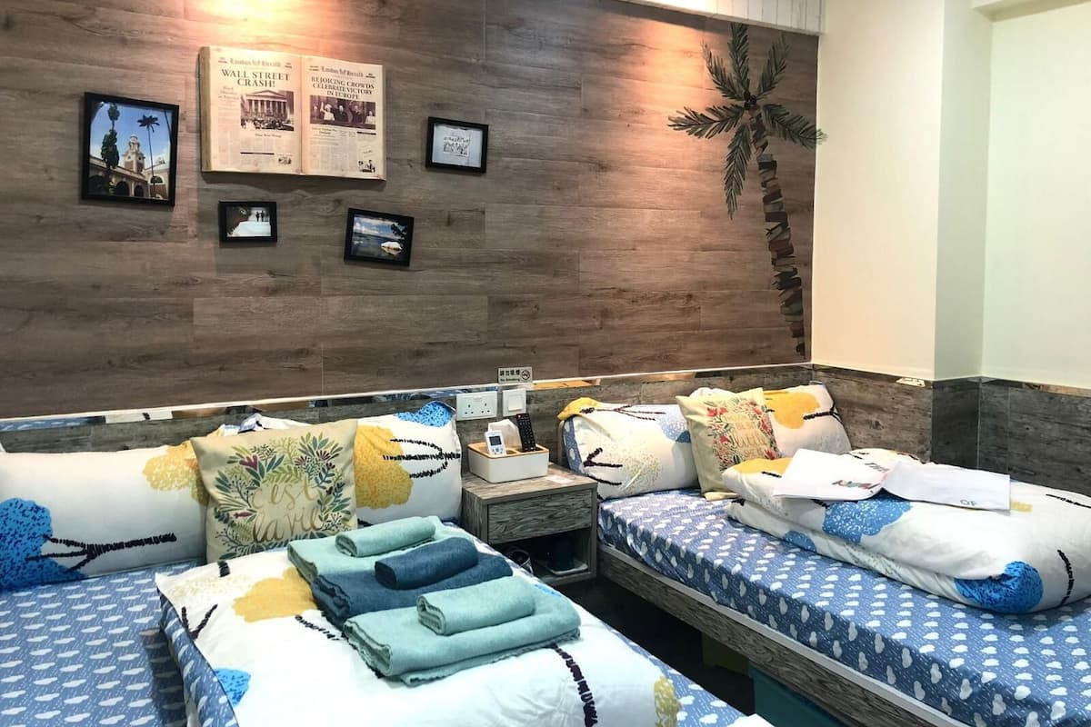 A hotel room with two beds, a wooden accent wall, and a small table with a phone and a sign.