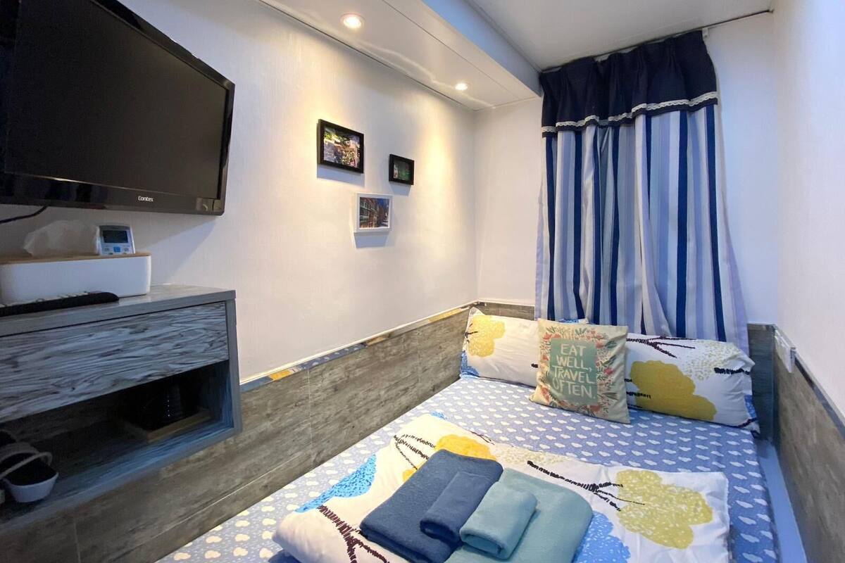 A bedroom with a bed, a TV mounted on the wall, and a window with curtains.