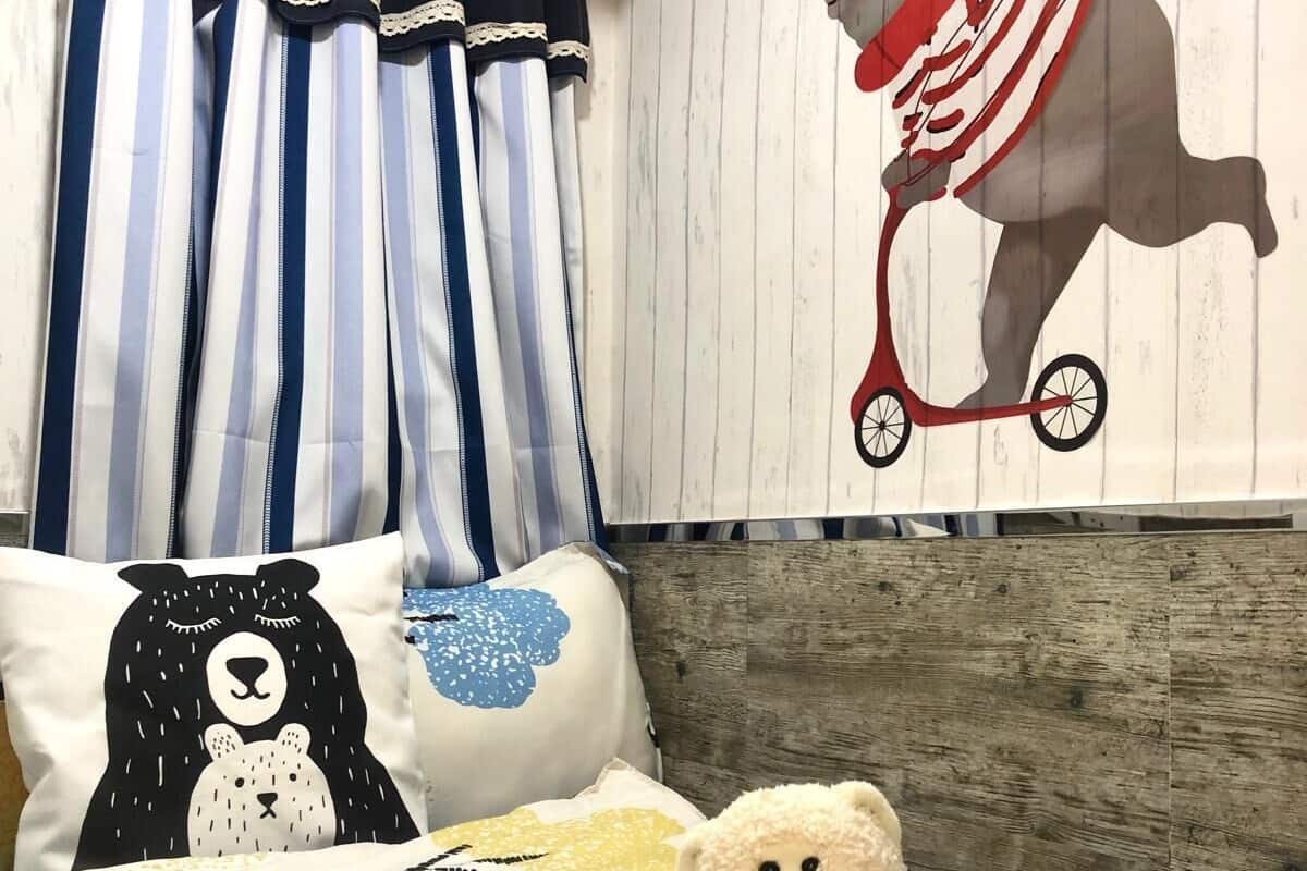 A bedroom with striped curtains, a wall mural of a bear on a tricycle, and a teddy bear on a bed.
